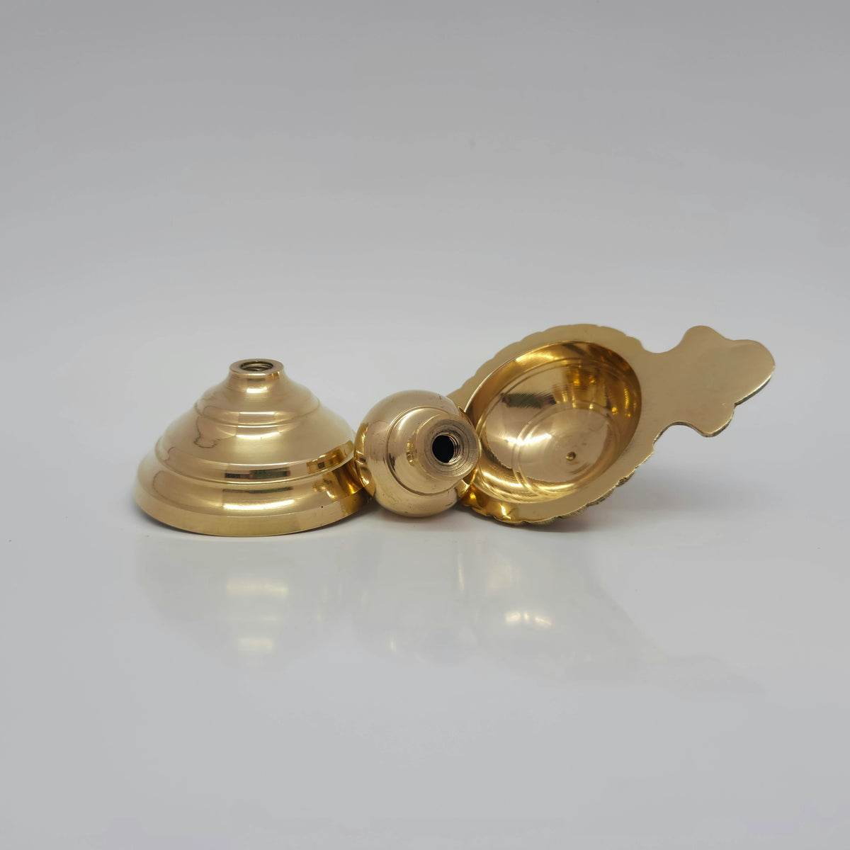Top-down presentation view showcasing the adjustable brass arati diya completely unscrewed into three separate parts—the oil basin with handle, central fluted stem pin, and flared base.