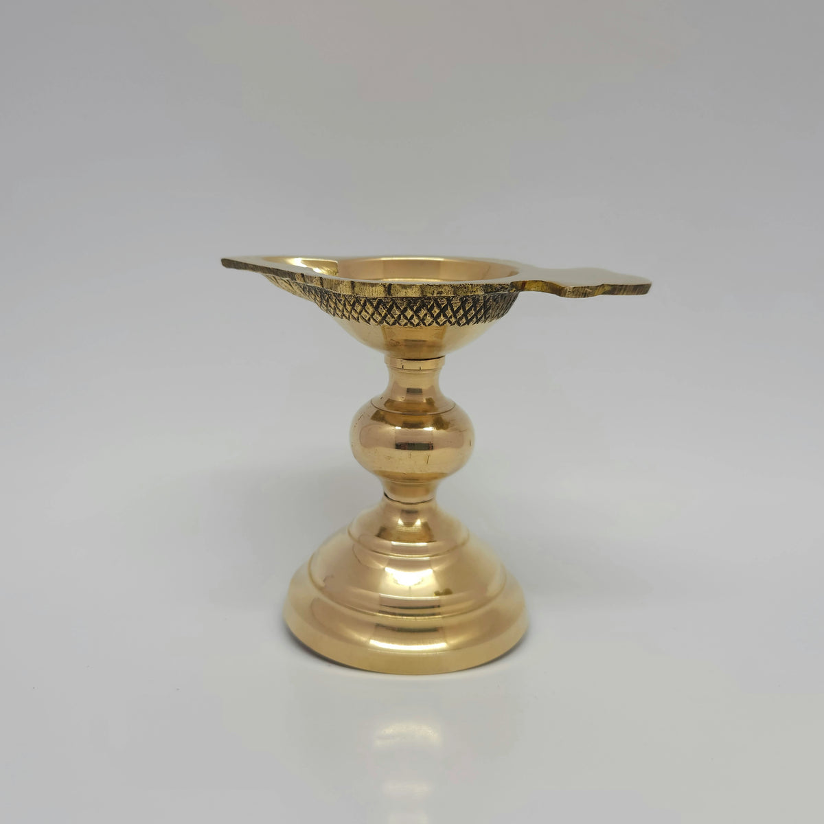 Rear standing perspective view of the tall pedestal brass arati lamp demonstrating the smooth high-gloss mirror finish along the base stem.
