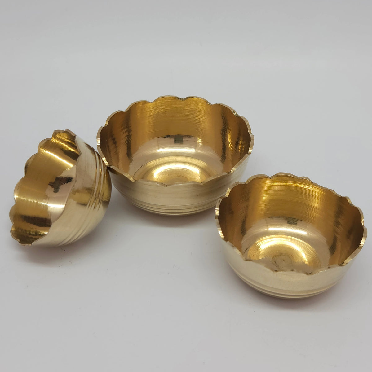 Three-quarter top perspective view demonstrating three individual brass bloom lotus katori cups clustered together with one tilted to show the polished inner basin