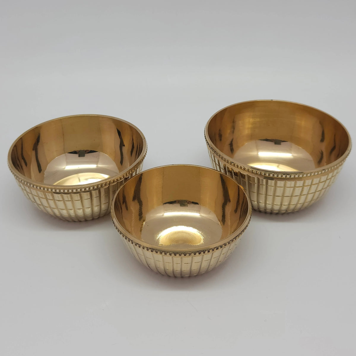 Top down angle view demonstrating three individual brass checked pattern pebble katori cups positioned together in a triangular group on a flat surface.