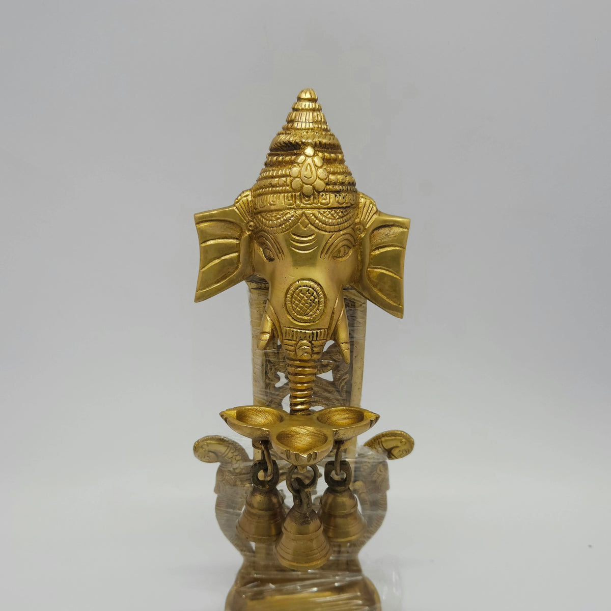 Close up front view of the antique brass Ganesha wall hanging lamp highlighting the sharp lines carved along the face and crown.