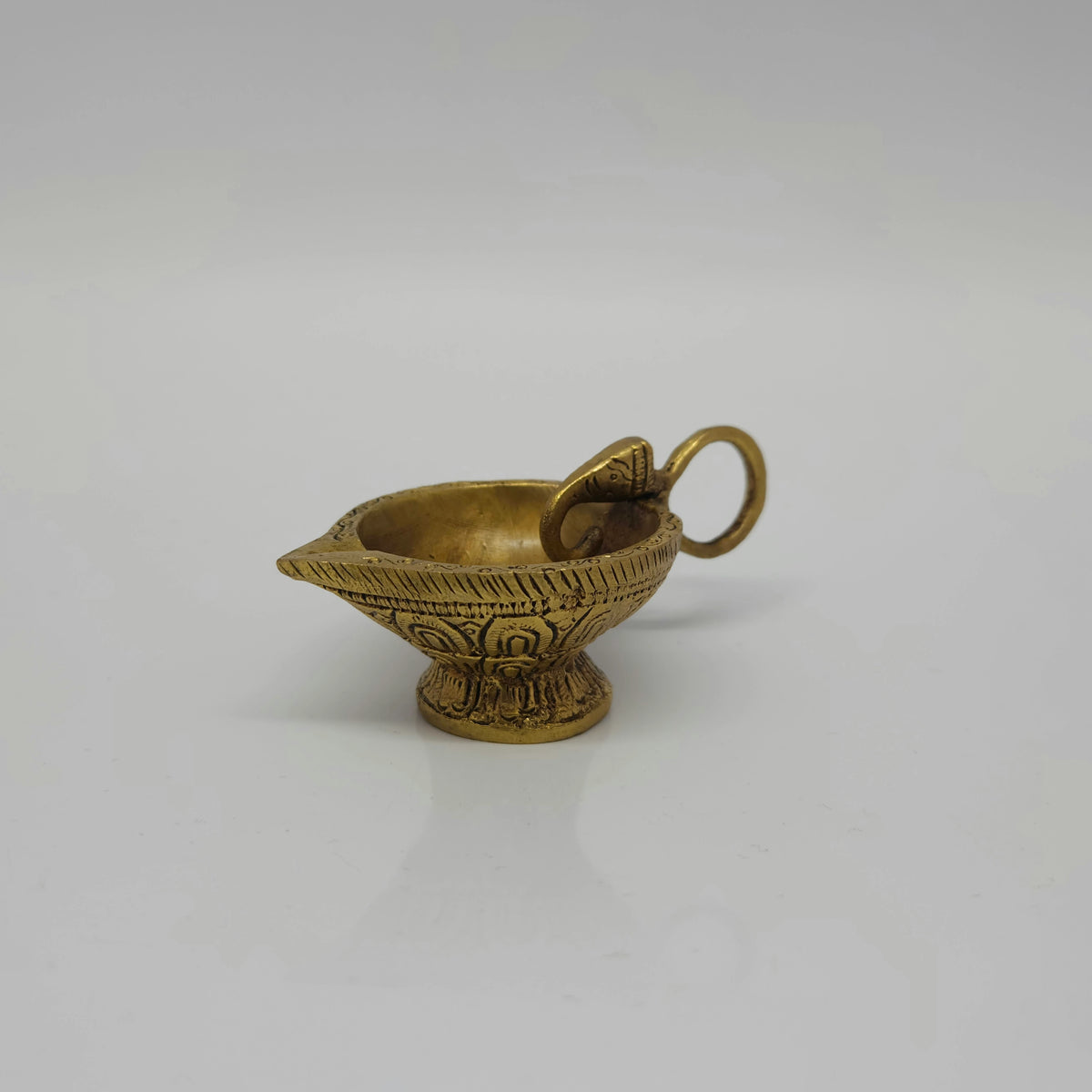Three quarter view of the 160g heavy brass handheld oil lamp highlighting the lotus petal carvings on the base and the elephant head connection.