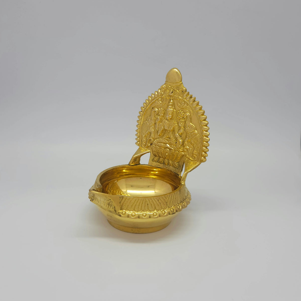 Three-quarter front left perspective view of the solid brass Kubera Gajalakshmi lamp showing the sharp vertical ridge lines on the outer rim.