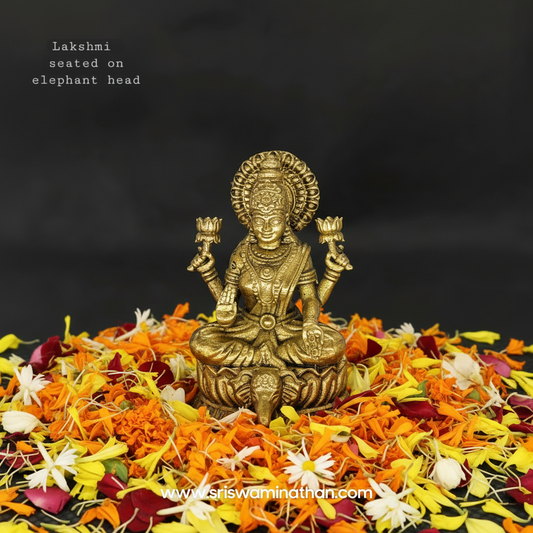Straight front view of the 4.5cm premium brass Lakshmi statue on an elephant head pedestal throne surrounded by fresh colorful flower petals for pooja room display by Sri Swaminathan and Co.
