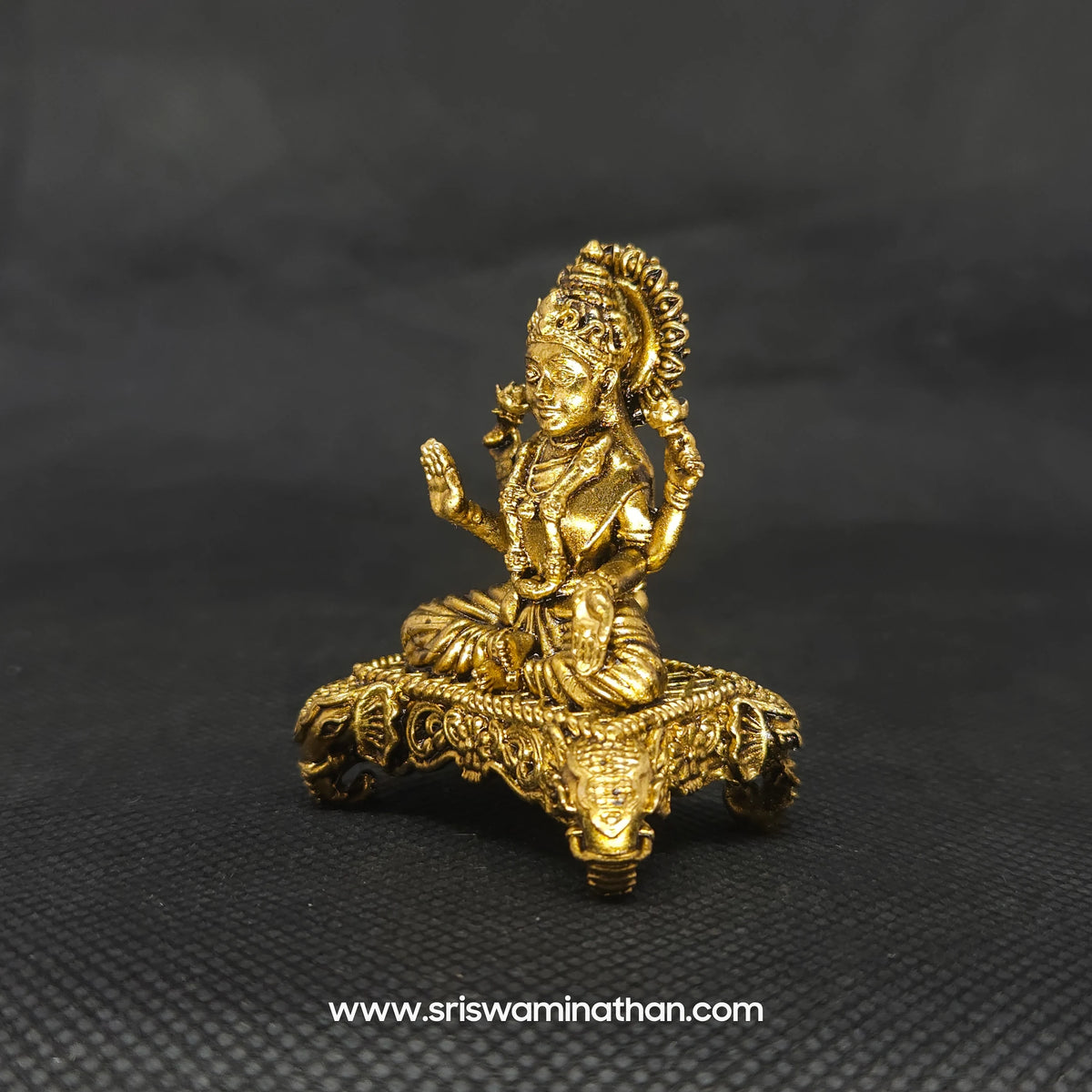 Three-quarter front left perspective view of the 5cm solid brass Lakshmi icon on a four-legged pedestal showing a durable dust-resistant surface needing only gentle liquid wipes.