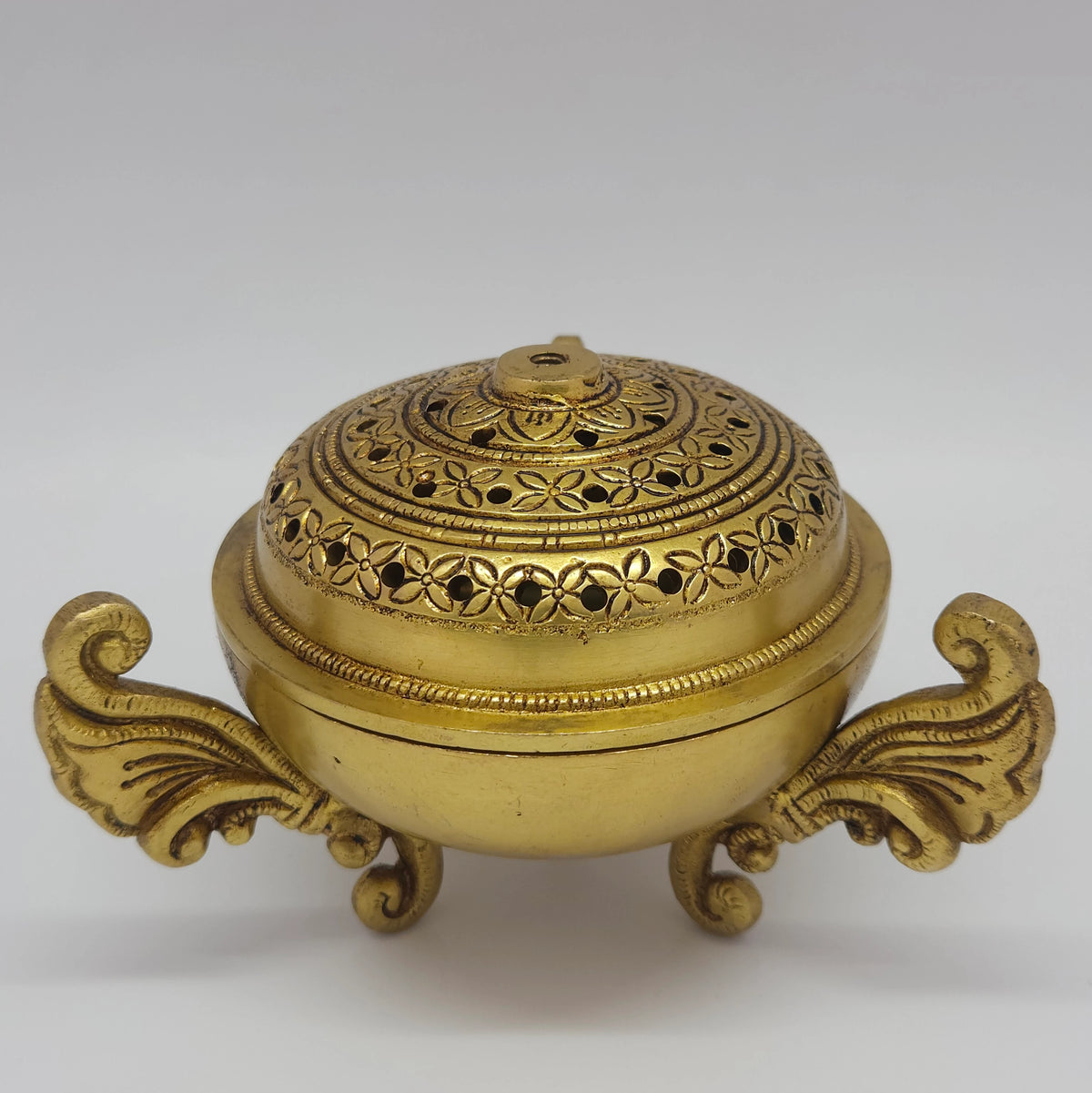 Three-quarter front perspective view of the premium brass peacock dhoop dhani showing the detailed perforated floral mesh lattice layout on the lid.
