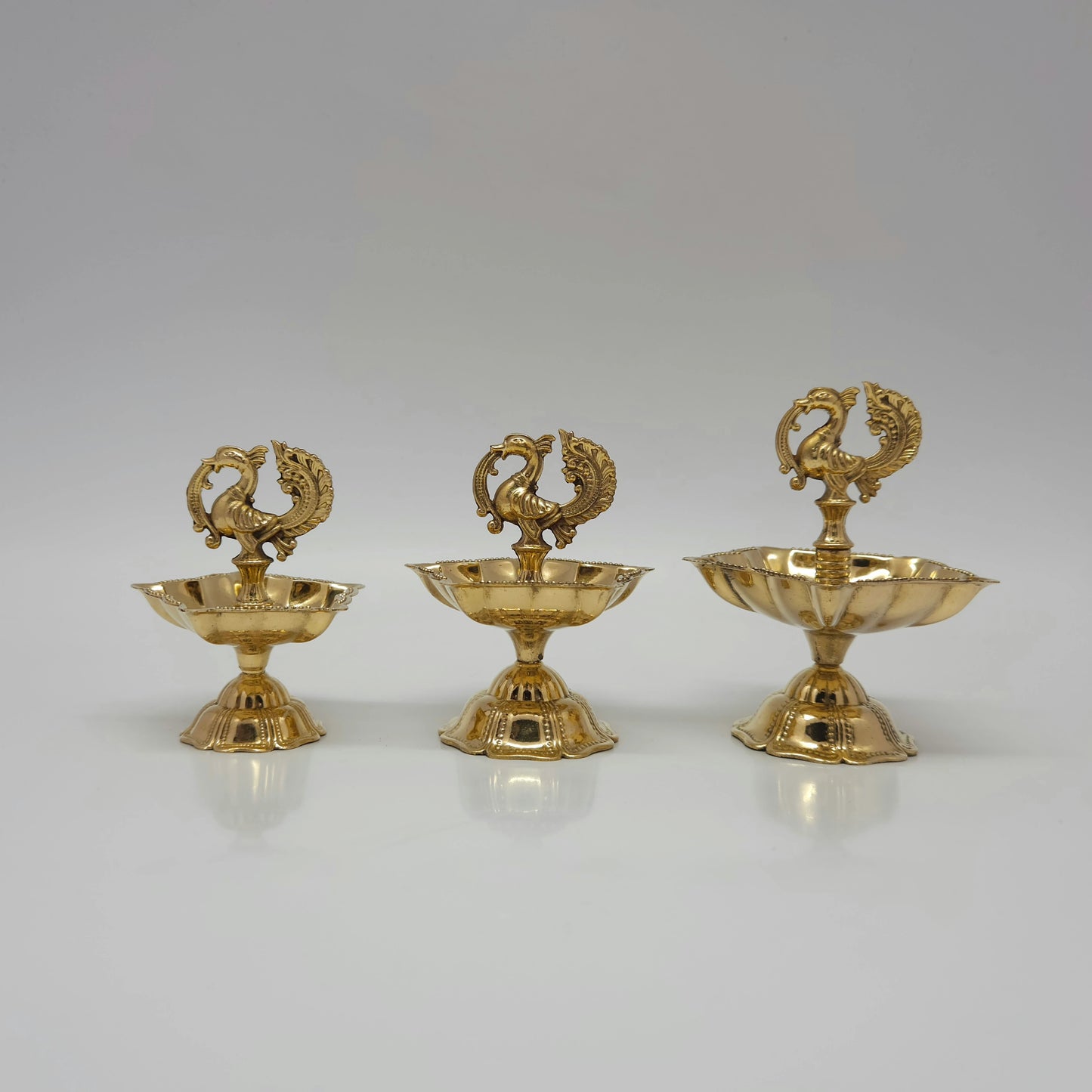 Three different sizes of pure brass peacock lamps standing side by side.