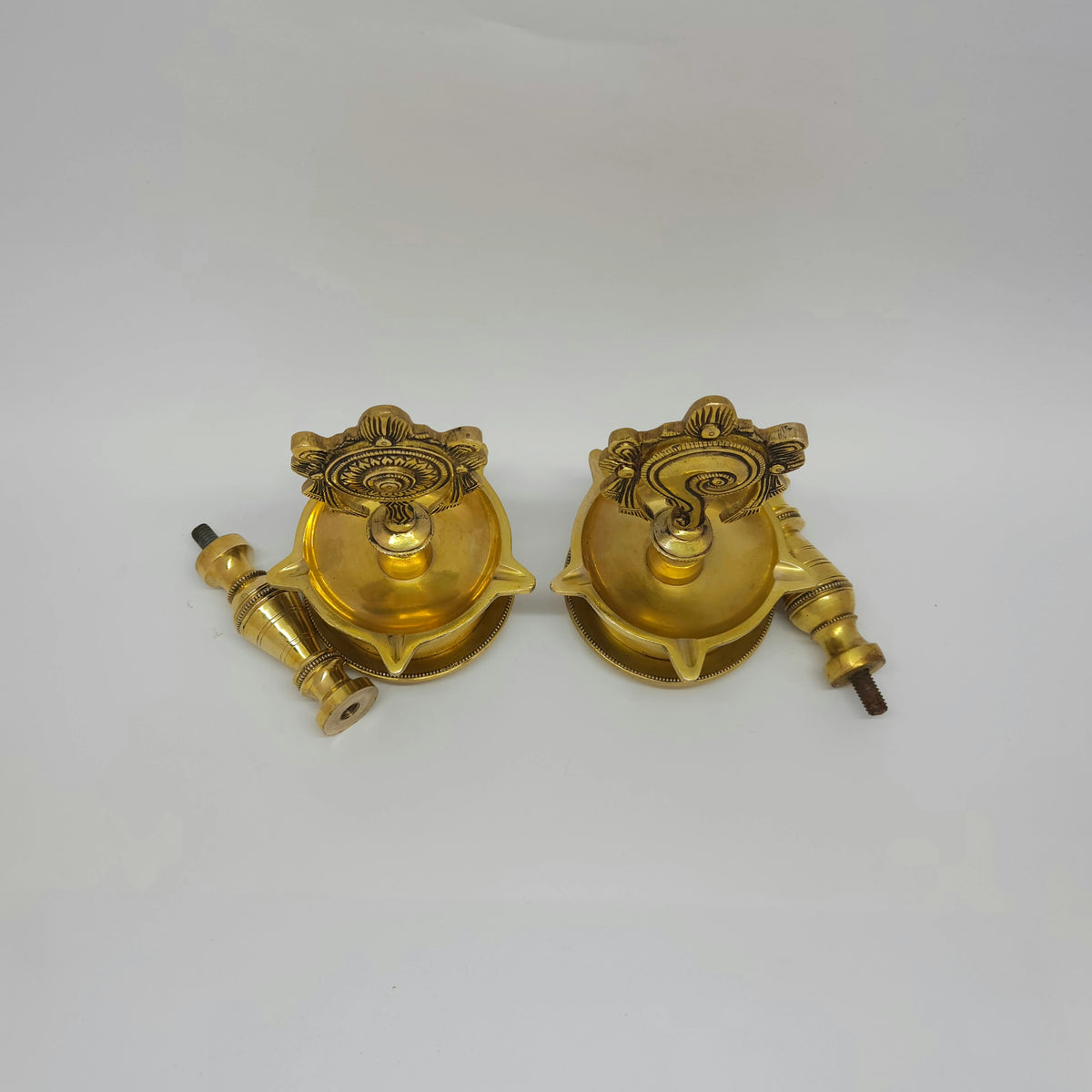 High angle top-down view of the detached brass Shanku and Chakra oil bowls resting next to their pedestal stems highlighting the wide 8.5cm basin diameters.