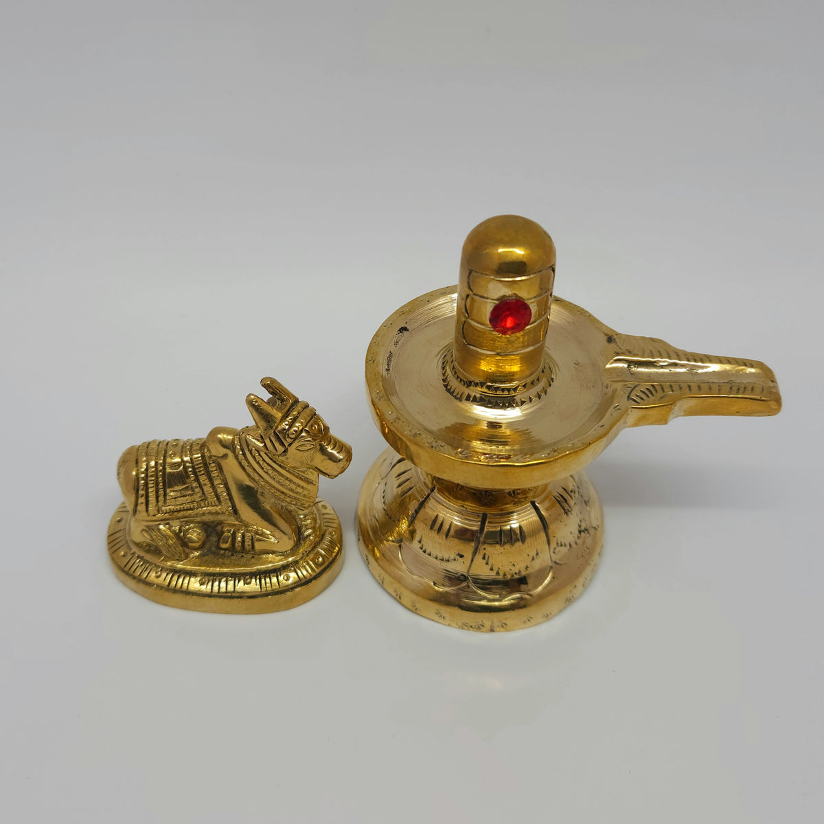 Three-quarter front left perspective view of the 9cm solid brass Shivling set showing the prominent red stone third eye alignment next to Nandi.