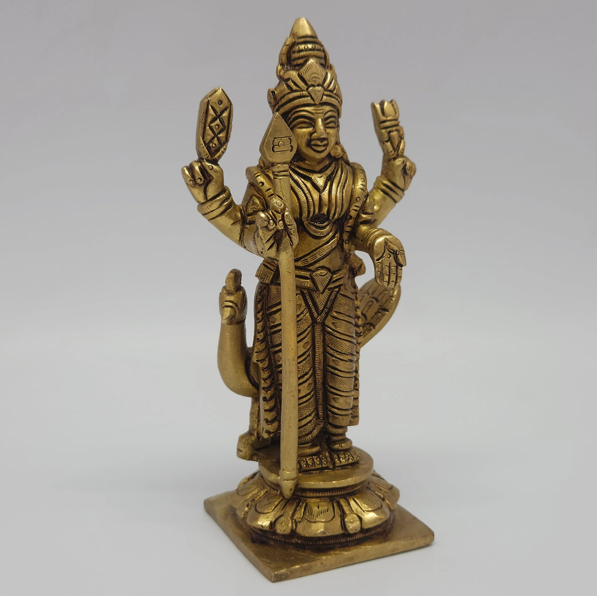  Low three-quarter front left profile view of the solid brass standing Murugan statue highlighting the tiered circular lotus peedam base platform.

