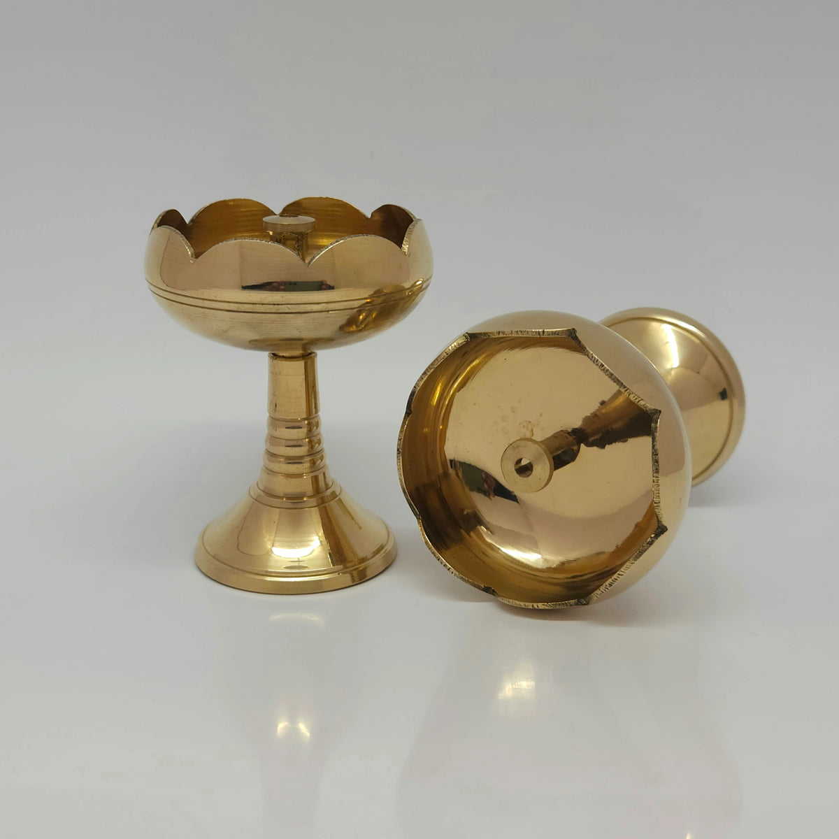 Angled view displaying one brass tall tulip diya standing upright next to another diya tilted back to reveal the clean circular base layout.
