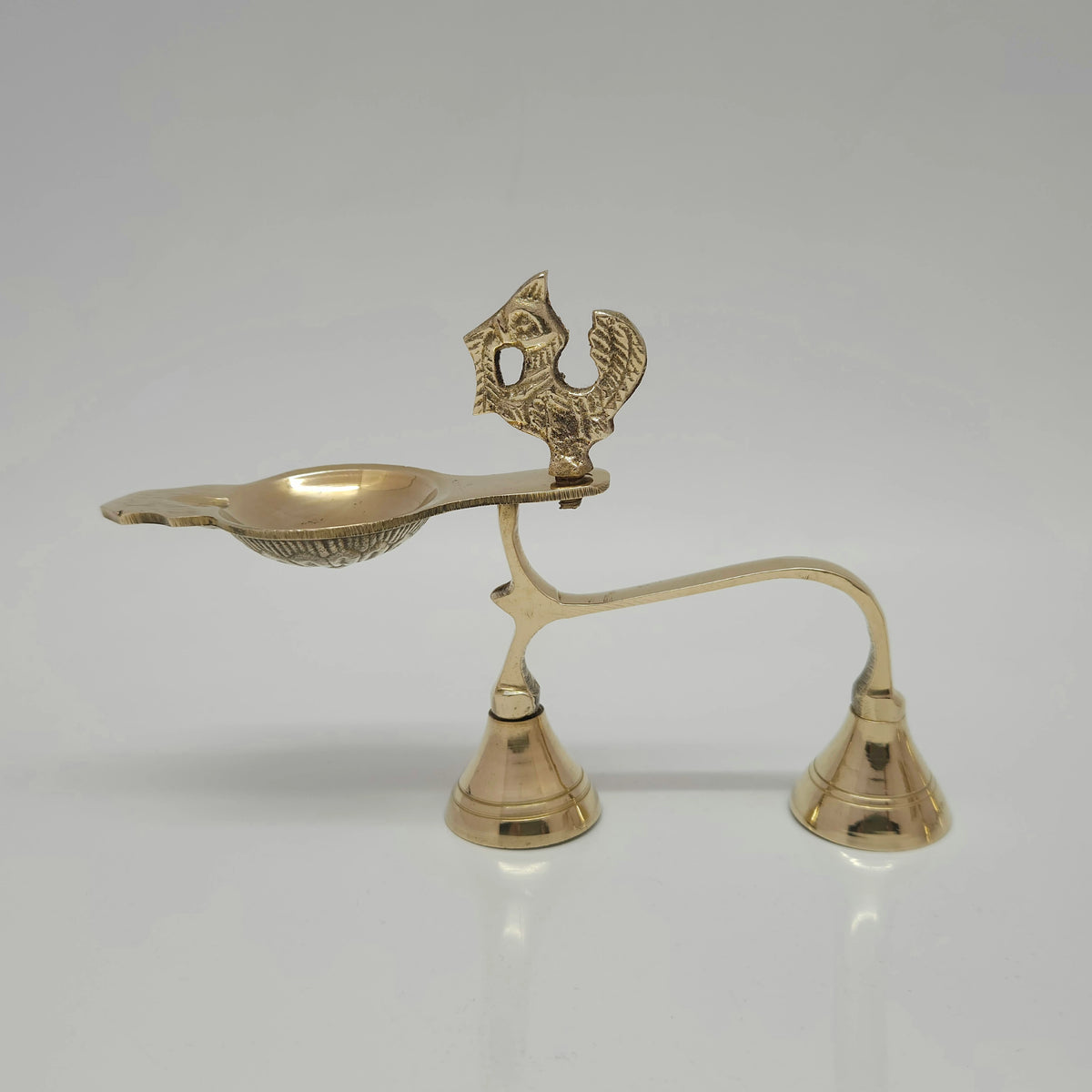 Right side profile view of a single solid brass handheld Annam aarti lamp showing the swan motif, shallow oil cup, and twin bell-shaped feet on a light grey background.