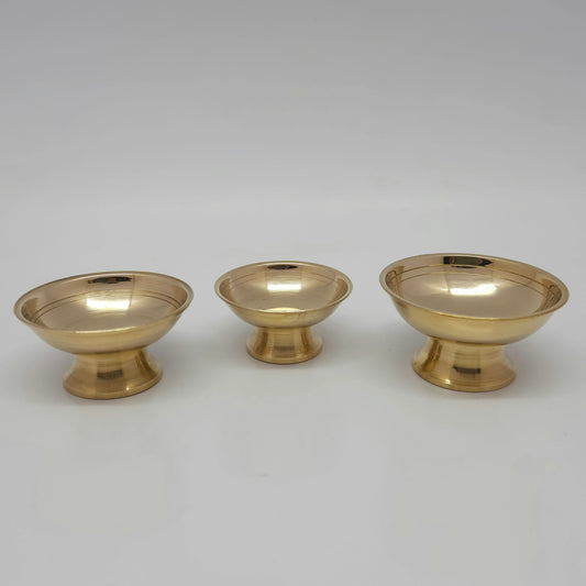 Front view of three size variants of pure glossy brass multipurpose offering bowls with pedestal bases lined up on a plain white background.