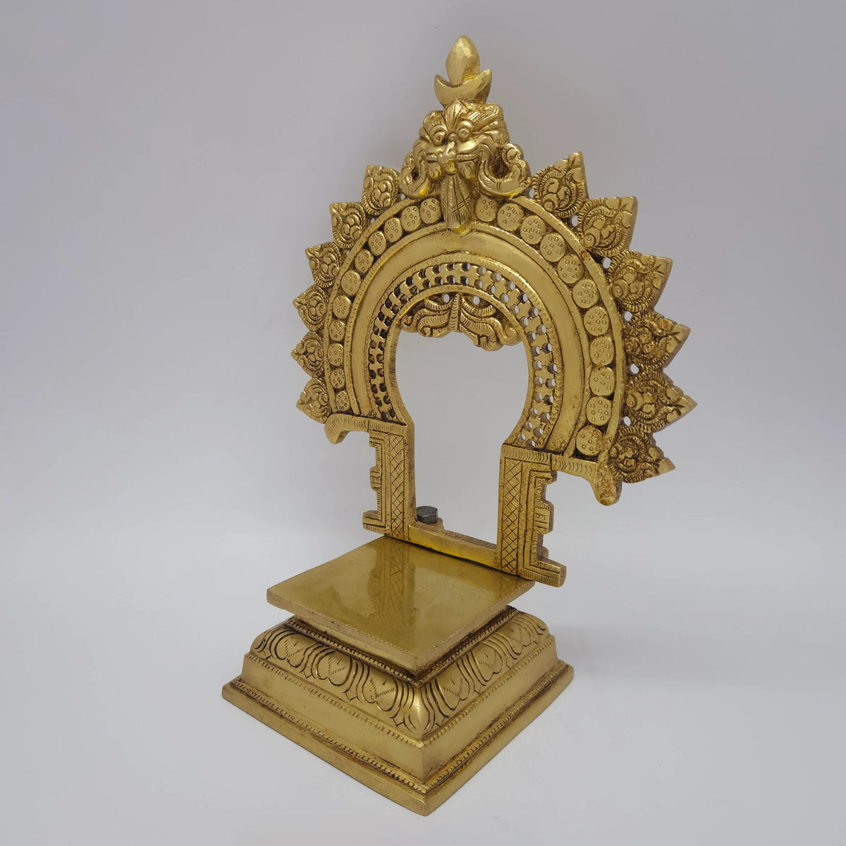 Three-quarter front right perspective view of the eleven inch brass prabhavali singhasan throne demonstrating the polished rectangular platform and chiseled flame archway border.