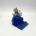 Lower three-quarter right perspective view of the translucent blue resin Ganesha idol sitting comfortably on his throne.