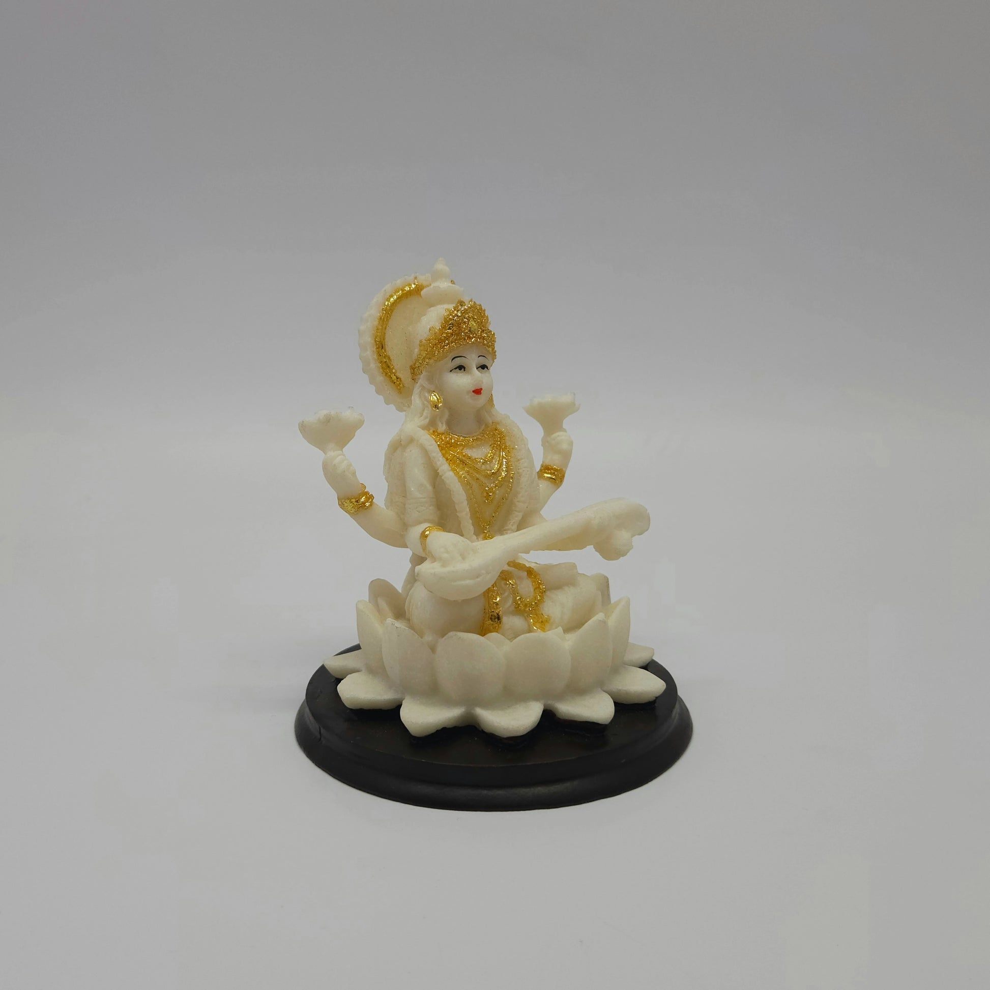 Angled front right look of the white poly-marble Saraswati figurine showcasing her hand-painted gold crown and layered lotus petals.