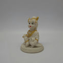 Angled front left perspective of the white resin child Krishna figurine highlighting the detailed white peacock sitting next to his foot.