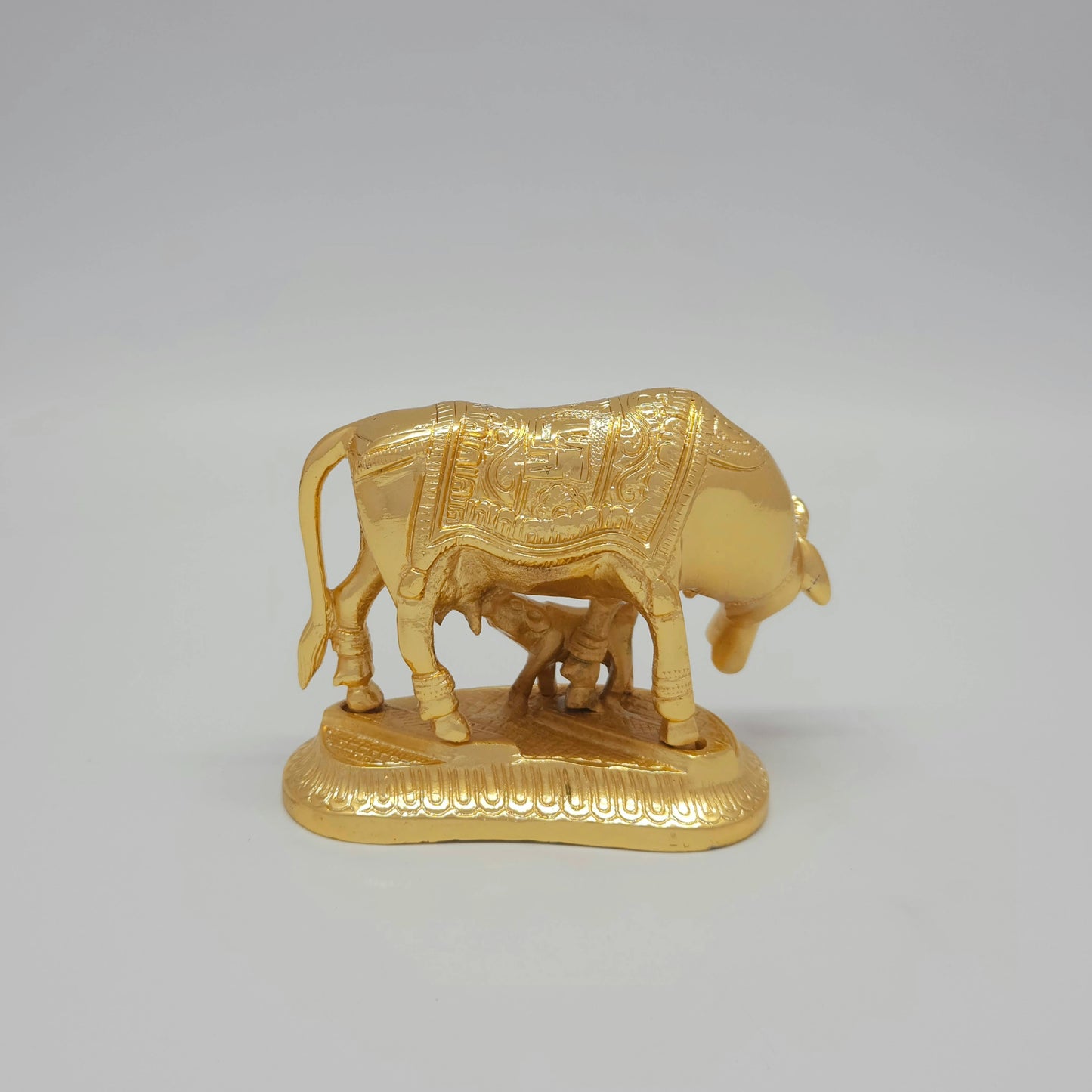 Full back view of the gold powder-coated solid brass Kamadhenu sculpture demonstrating the sacred traditional Swastika symbol engraved on the rear base platform.