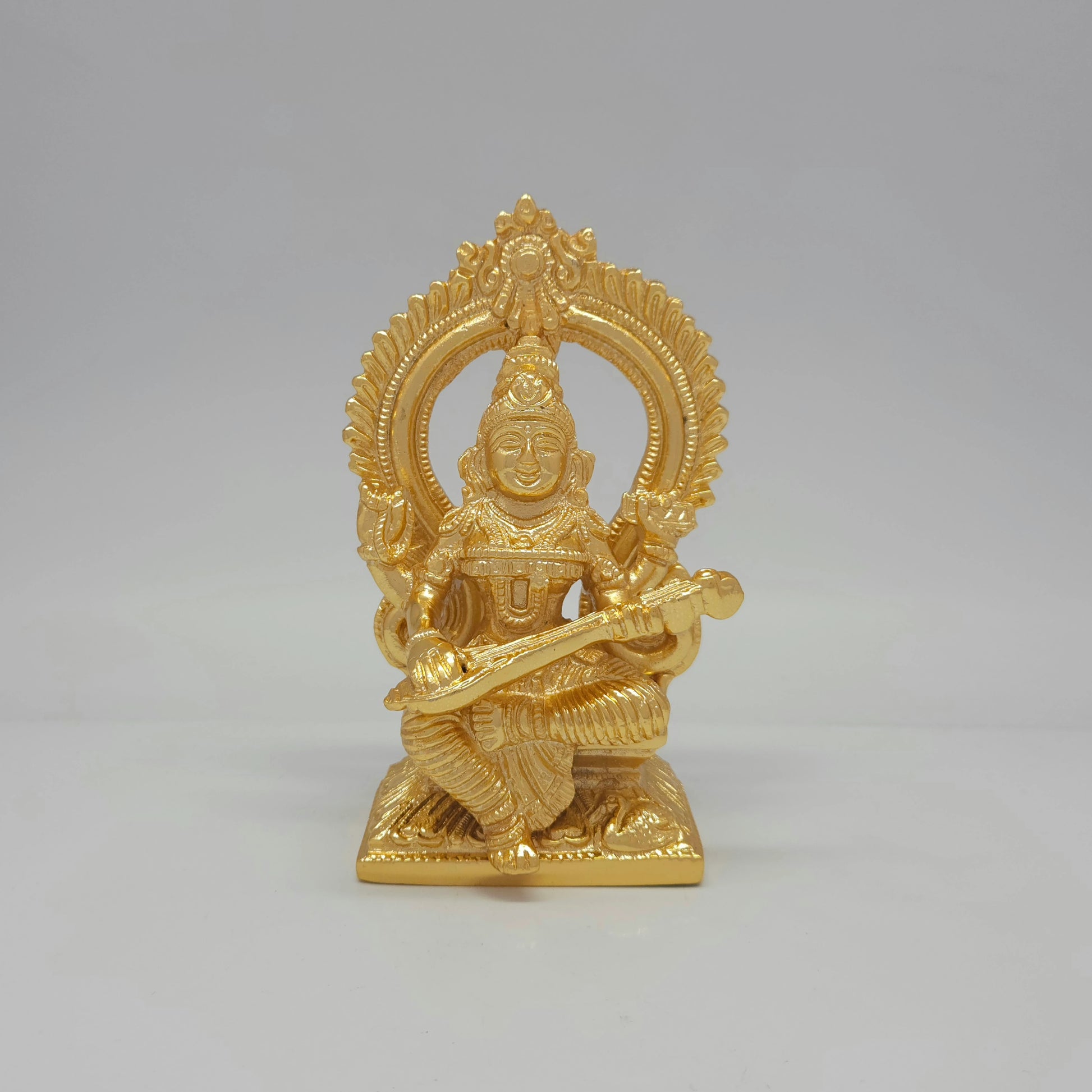 Front view of a 14.5cm premium gold powder-coated solid brass Goddess Saraswati statue playing a veena with a traditional halo arch by Sri Swaminathan and Co.