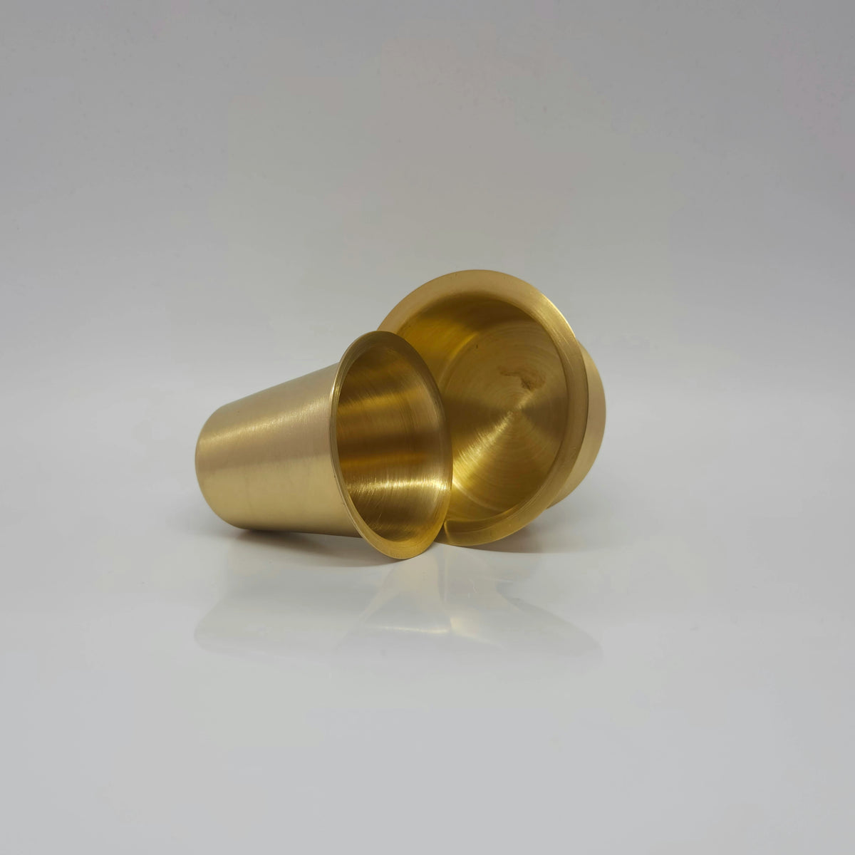 Lying profile view of the 175g matte finish brass coffee tumbler showing the inside base metal texture next to the davara cup.