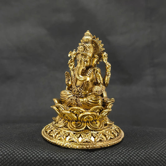 Three-quarter front left perspective view of the two and a half inch brass Ganesha statue on a round lotus peedam highlighting the sharp chiseled lines of his traditional weapon attributes.
