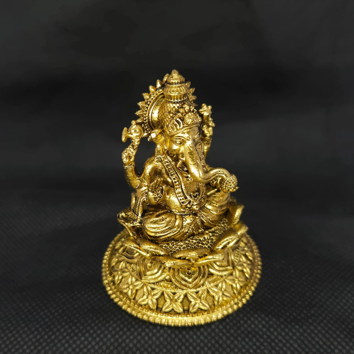  Three-quarter front right perspective view of the two and a half inch brass Ganesha statue showcasing his prominent fat abdomen and the detailed modak sweet cradled in his front left hand.
