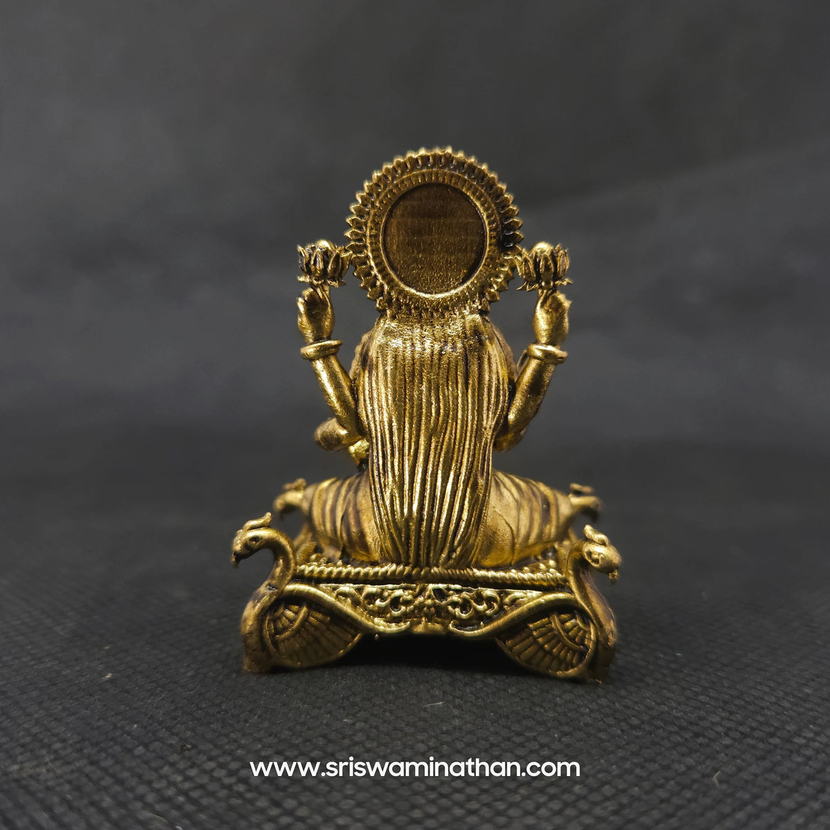 Direct straight back view of the solid brass Lakshmi statue on a hamsa throne demonstrating the detailed rear surface of the sunburst halo crown and back hair arrangement.
