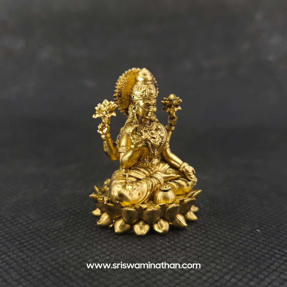 hree-quarter front left perspective view of the two and a half inch brass Lakshmi statue in her real form highlighting her detailed ornaments and the deep three-dimensional thickness of the casting.
