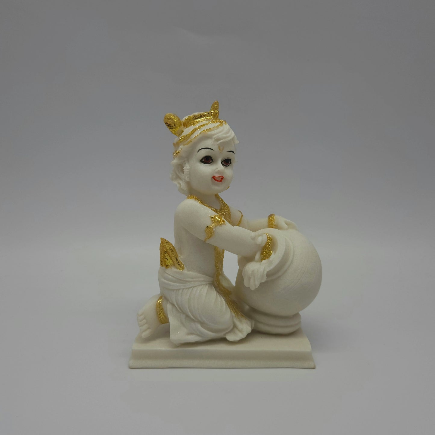 Straight front look of the white poly-marble Bal Krishna sculpture highlighting his golden crown ornaments and expressive eyes.