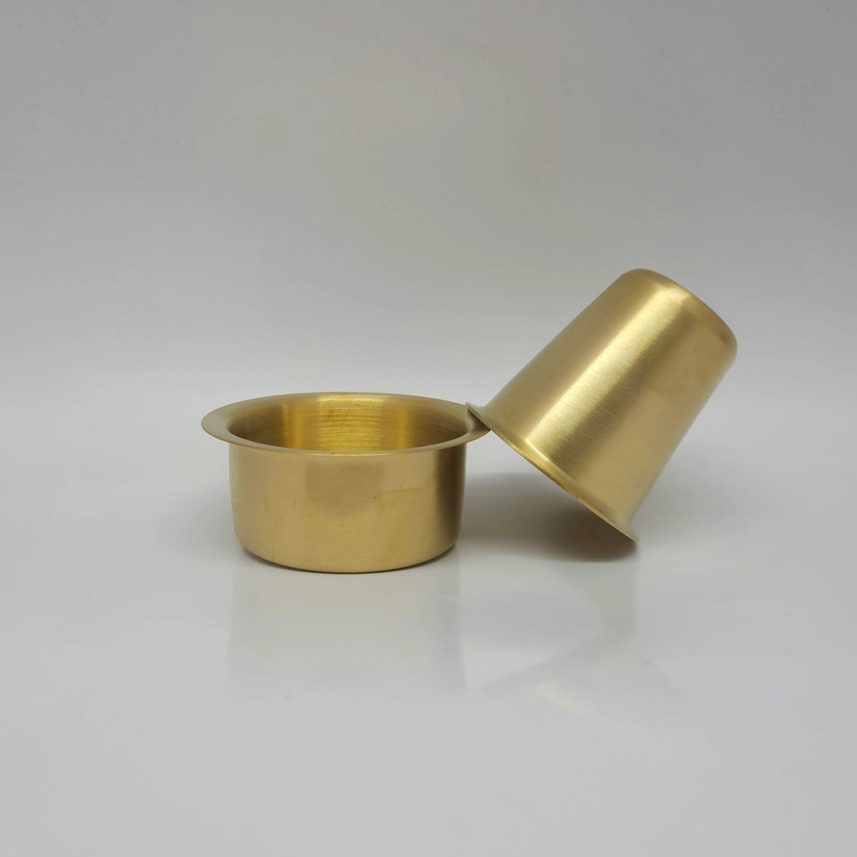 Side look of the heavy matte finish brass coffee tumbler resting sideways on the edge of the open davara cooling bowl.