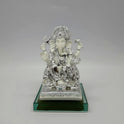 Front view of a 17.5cm metallic silver paint and satin white finish resin Ganesha statue on an emerald glass base by Sri Swaminathan and Co