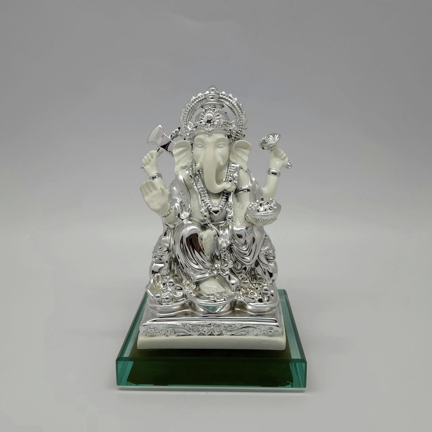 Front view of a 17.5cm metallic silver paint and satin white finish resin Ganesha statue on an emerald glass base by Sri Swaminathan and Co