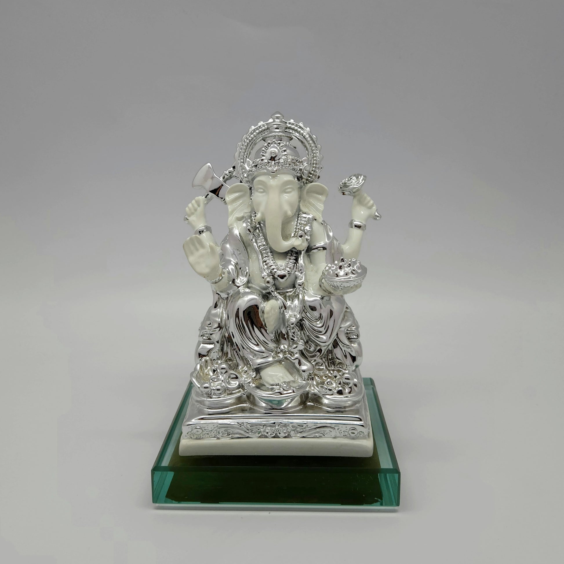 Front view of a 17.5cm metallic silver paint and satin white finish resin Ganesha statue on an emerald glass base by Sri Swaminathan and Co