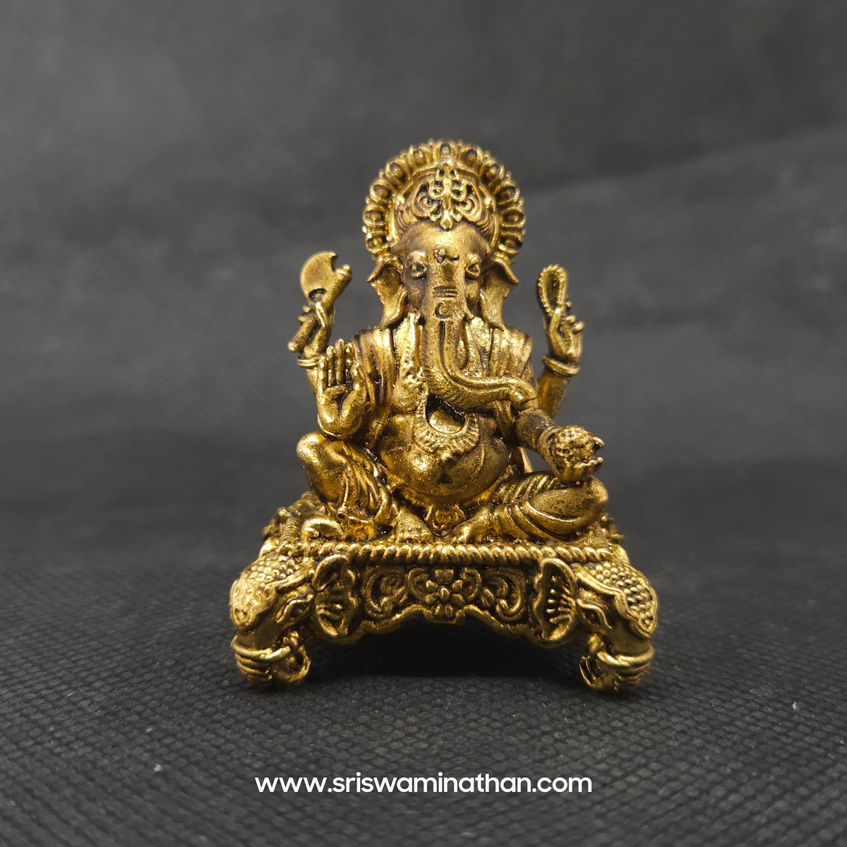Straight front view of the premium solid brass Ganesha statue showing the Lord with a veer thilak holding a laddu on a four-sided elephant head throne base by Sri Swaminathan and Co.