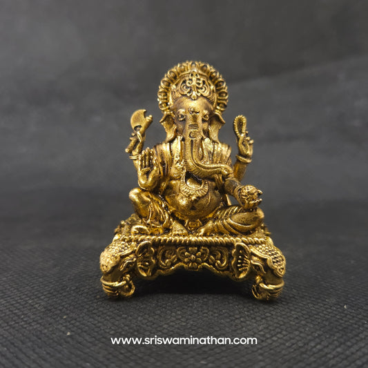 Straight front view of the premium solid brass Ganesha statue showing the Lord with a veer thilak holding a laddu on a four-sided elephant head throne base by Sri Swaminathan and Co.