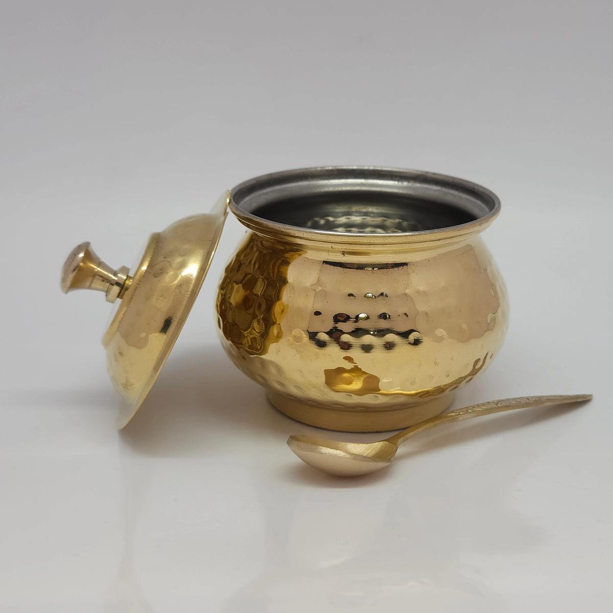 Three-quarter top perspective view of the polished brass hammered ghee pot in glossy finish showing the detailed dimple texturing and separate lid.
