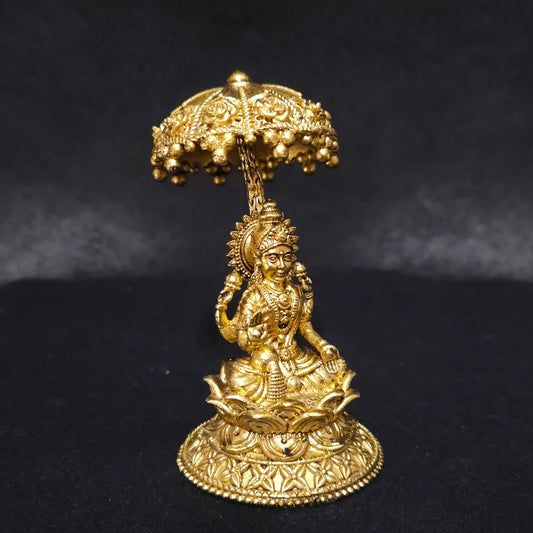 Three-quarter front left perspective view of the solid brass Lakshmi statue with a royal canopy highlighting the chiseled umbrella stem and the deep thickness of the solid casting.