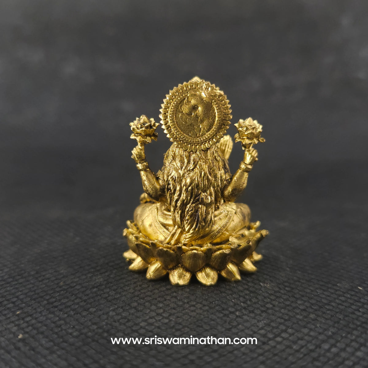 Direct straight back view of the solid brass Lakshmi statue in her real form demonstrating the detailed rear surface of the sunburst halo crown and back hair curls over the round base.
