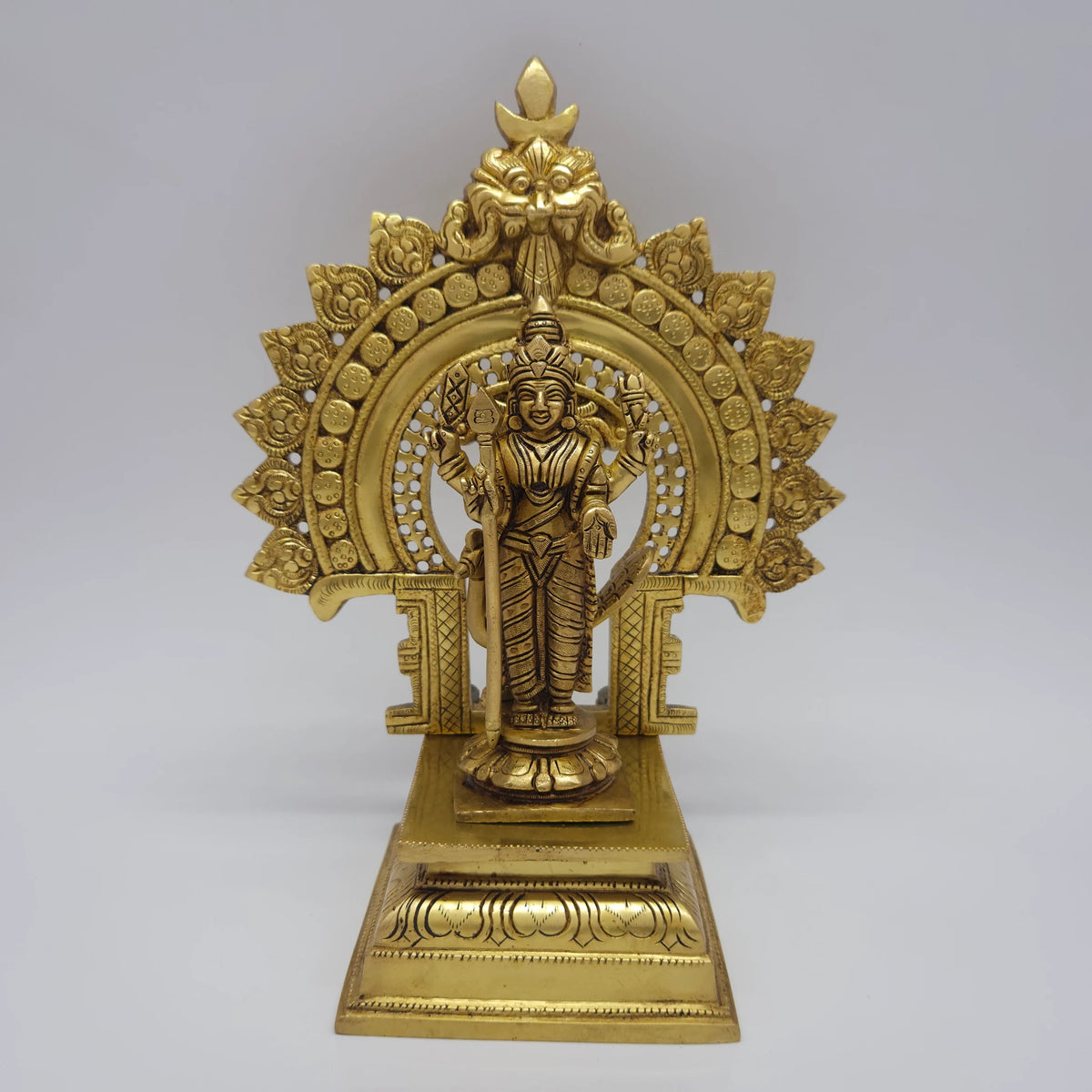 Direct straight front view of the premium solid brass Lord Murugan statue holding his sacred vel while placed on the antique finish prabhavali singhasan throne by Sri Swaminathan and Co.