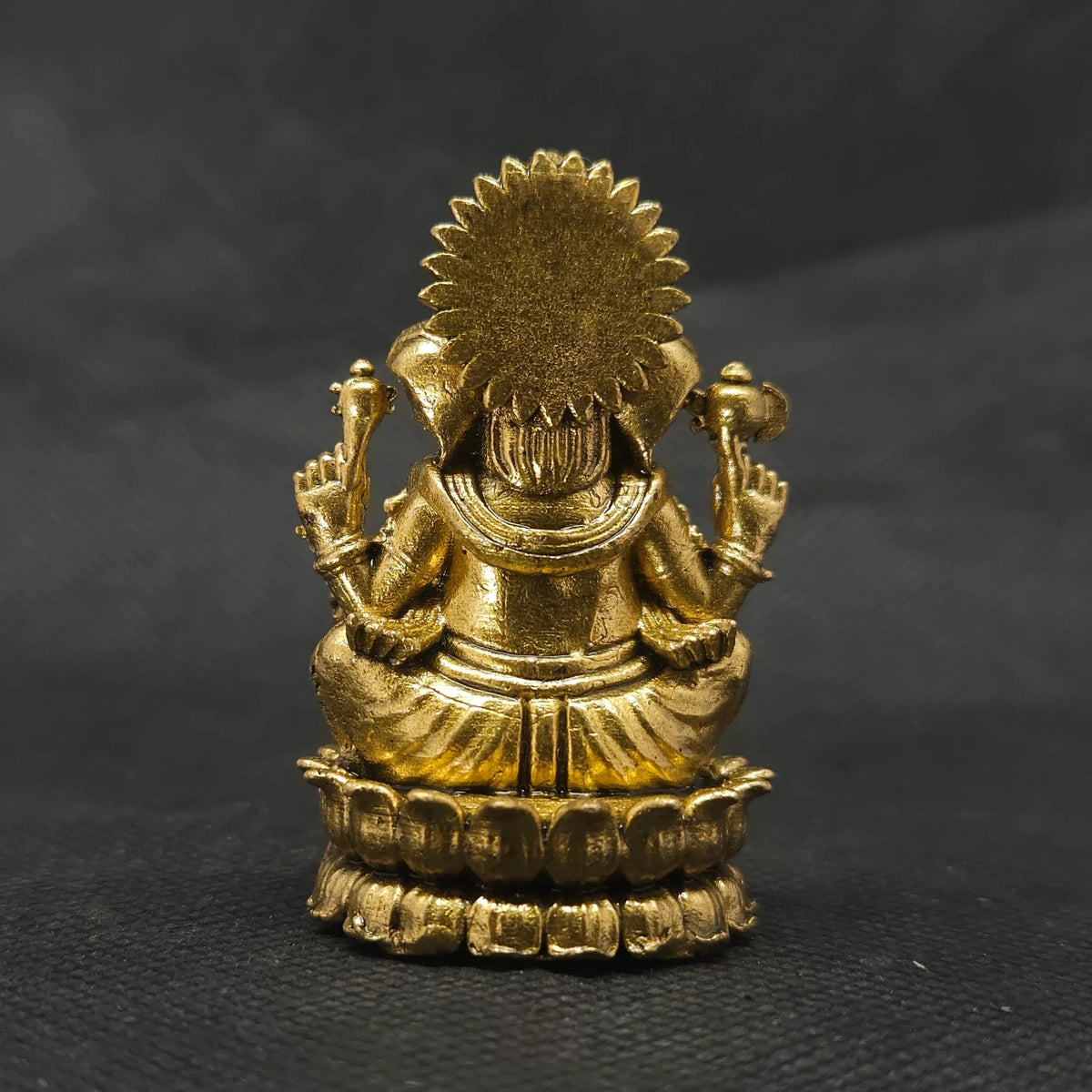 Direct straight back view of the solid brass Ganesha statue demonstrating the detailed rear surface of the sunburst halo crown armor and back contours of the round lotus seat.