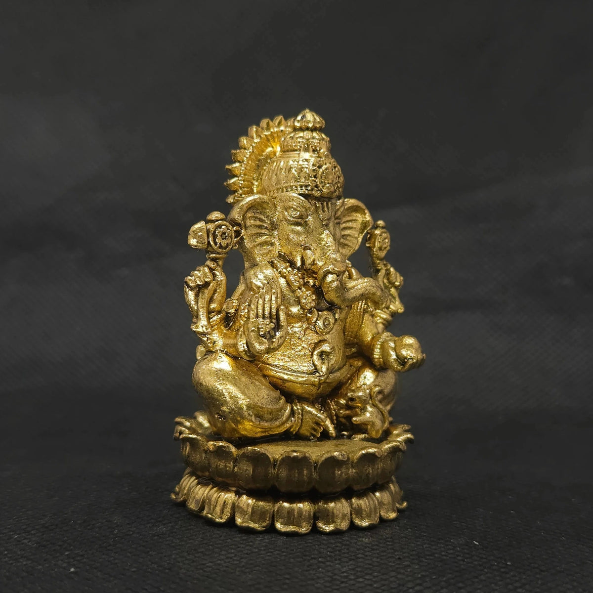 Three-quarter front left perspective view of the brass Ganesha statue highlighting the chiseled lines of his traditional weapon armors and the deep three-dimensional thickness of the casting