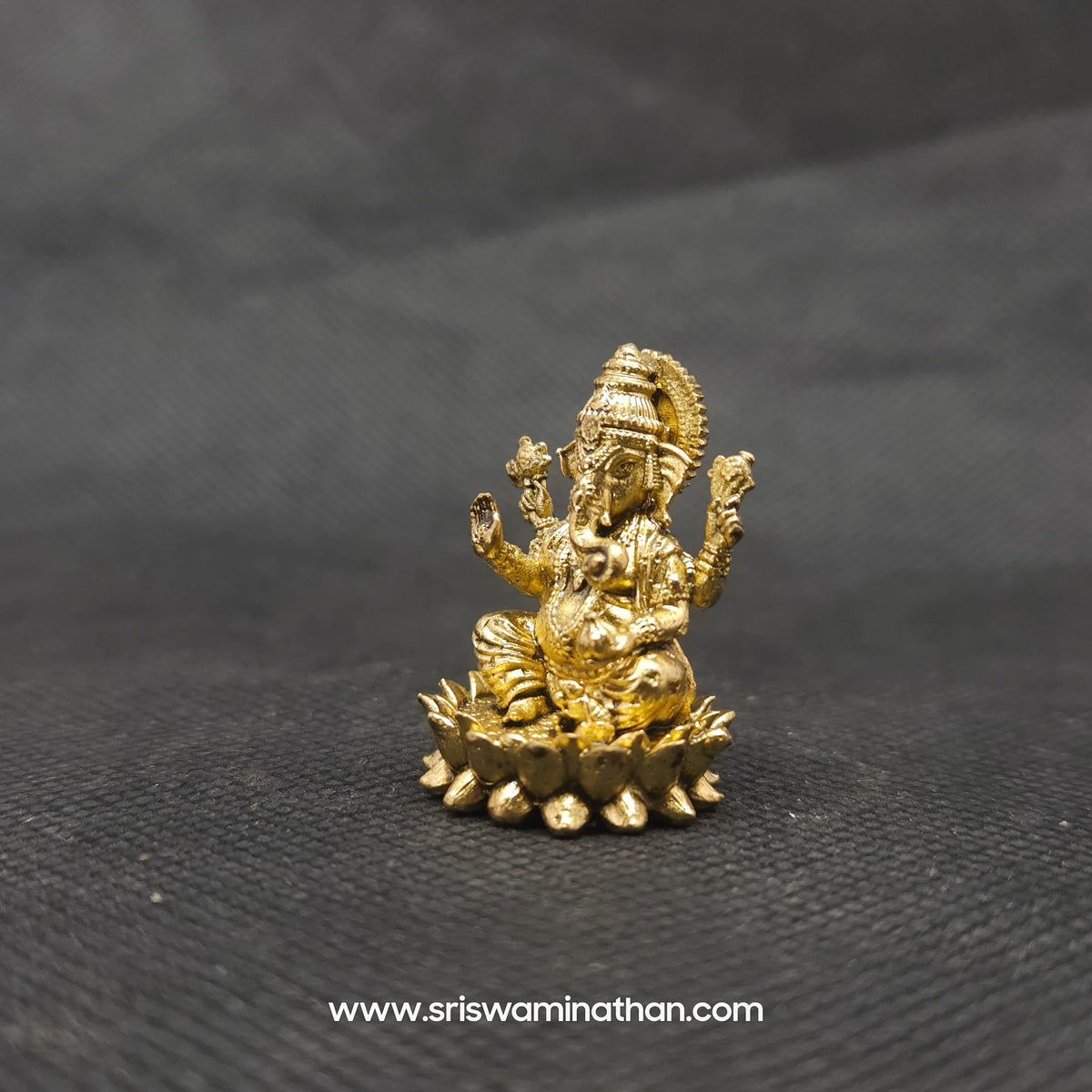 Three-quarter front right perspective view of the one inch brass Ganesha statue showcasing his prominent fat abdomen, the detailed modak, and Mooshikan seated on the round lotus edge.
