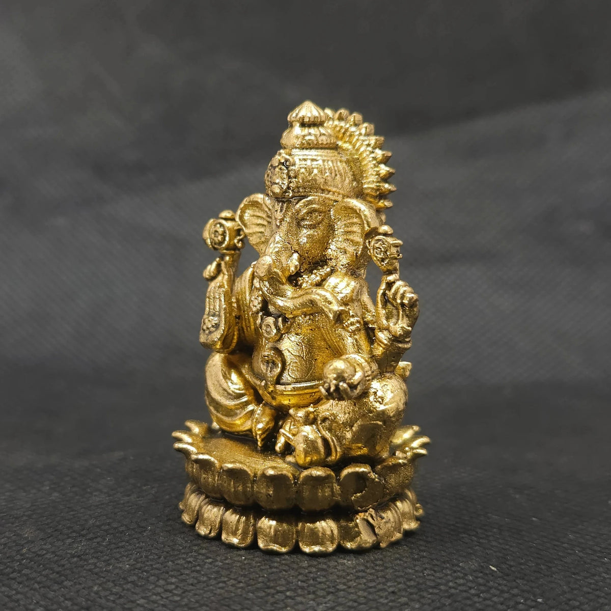 Three-quarter front right perspective view of the brass Ganesha statue showcasing his prominent fat abdomen, the detailed modak, and Mooshikan seated on the round lotus edge.