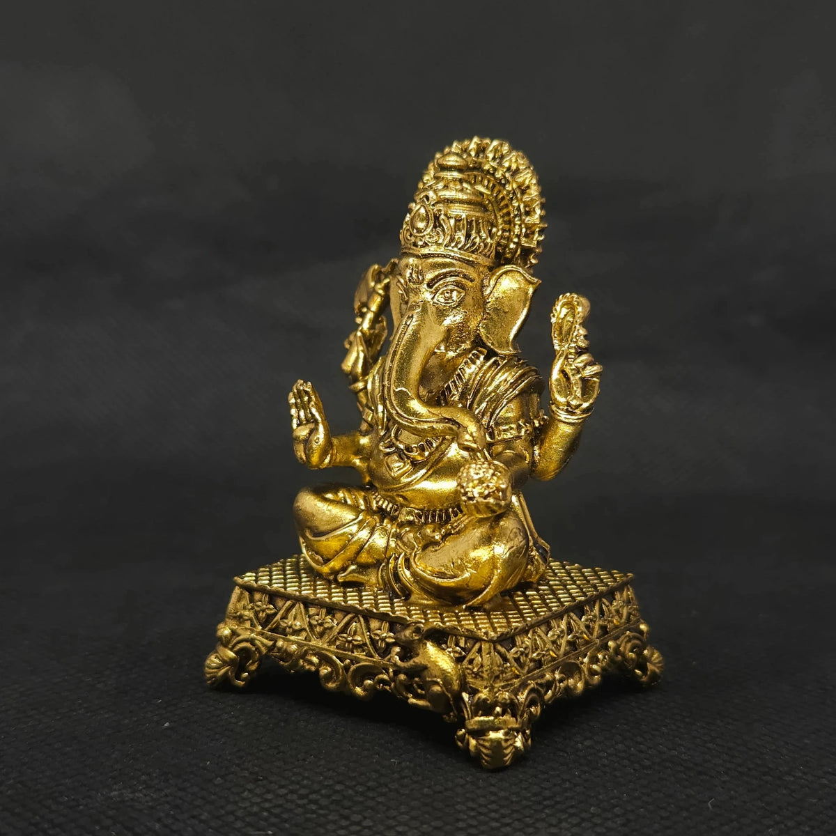 Forty five degree angle front left perspective view of the solid brass Ganesha statue on an ornate square peedam base showcasing the three-dimensional weapon details