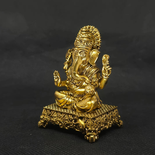 Forty five degree angle front left perspective view of the solid brass Ganesha statue on an ornate square peedam base showcasing the three-dimensional weapon details