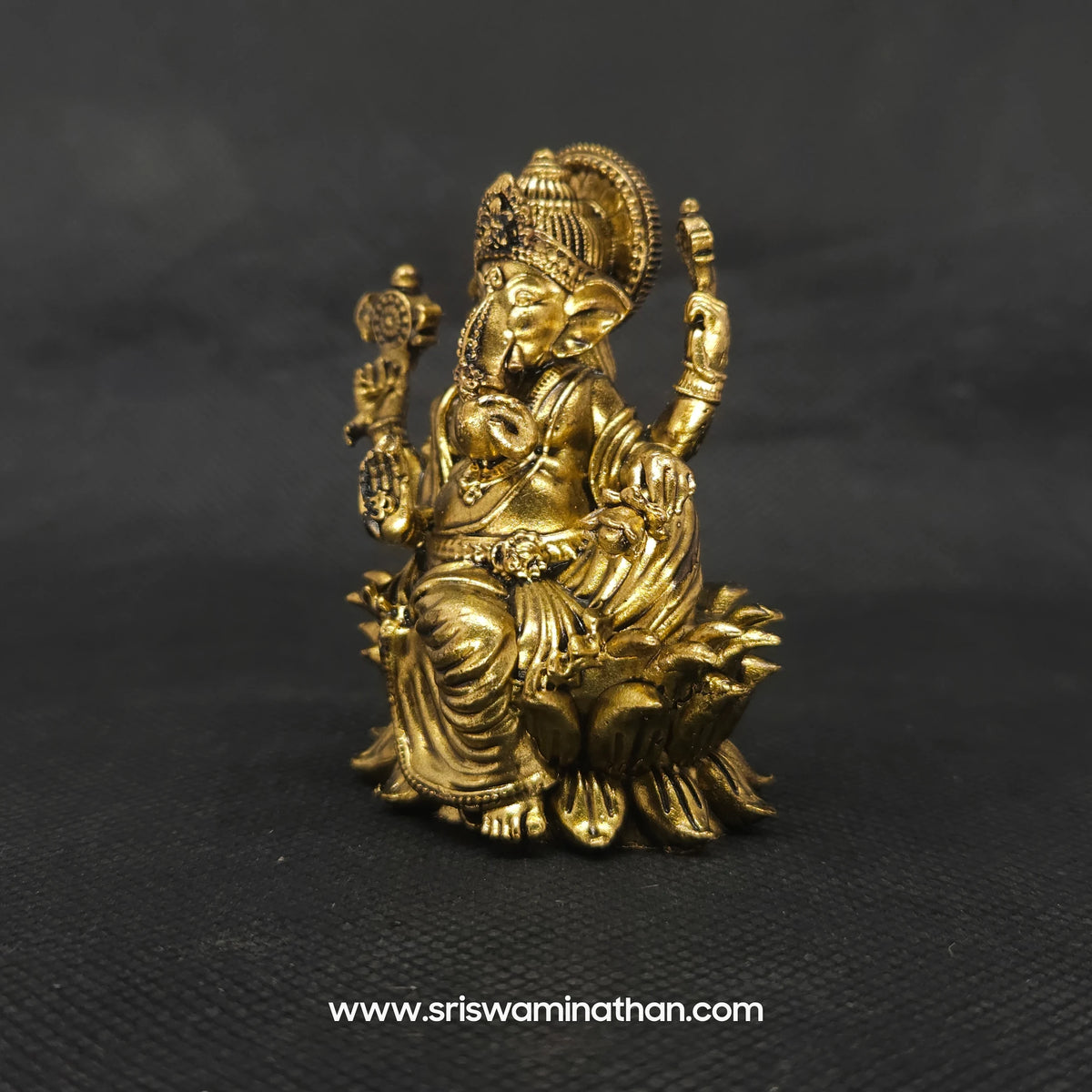 Three-quarter front left perspective view of the solid brass seated Lalita Ganapati statue highlighting the sharp detailed lines of the attributes and the deep three-dimensional thickness of the casting.
