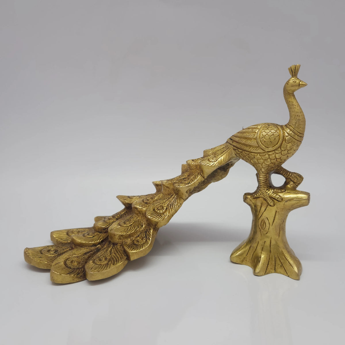 Low three-quarter front left profile view of the solid brass small peacock decor statue showcasing the detailed cascading lines of his long tail feathers.