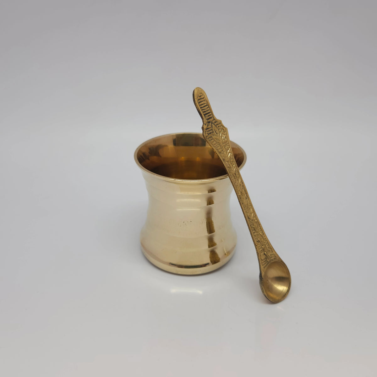 Three-quarter front view of the big size pure brass panchapatra cup shown with its structural long ritual spoon resting gracefully inside the vessel