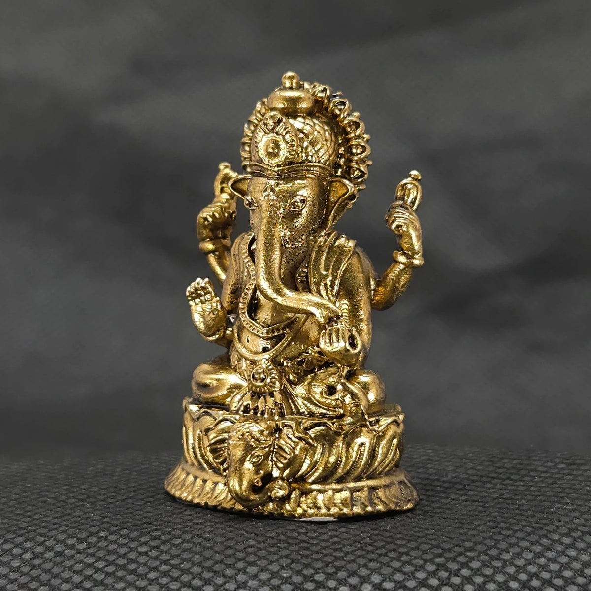 Three-quarter front right perspective view of the one point seven five inch brass Ganesha statue showcasing his prominent fat abdomen and the central elephant face profile on the lotus edge