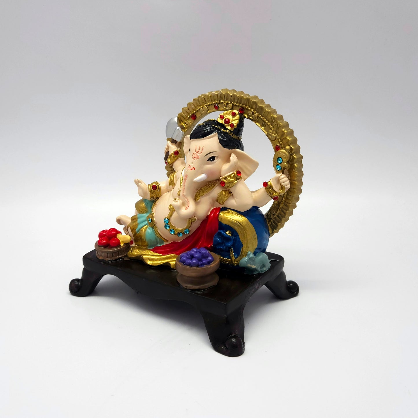 Side-angle view of a resting Ganesha idol showing the royal blue cushion details and bright red drapery accents